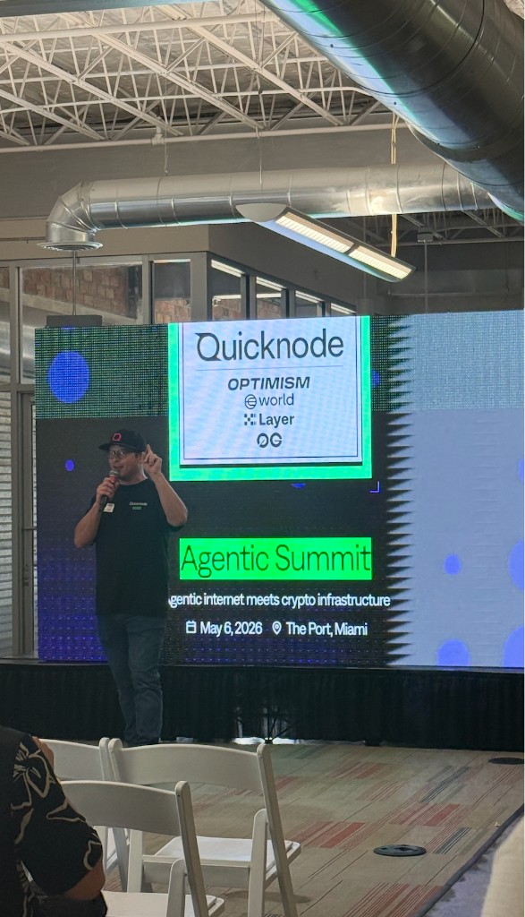 Speaker on stage at Agentic Summit Miami with QuickNode and sponsor logos, May 6 2026